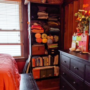 Photo of a tall black bookcase, filled with books, sweaters and yarn.